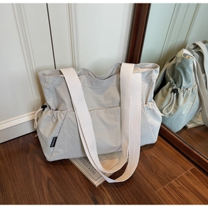 Detail of beige canvas tote bag with side drawstring ruffles and brand logo on wooden floor