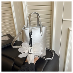 Detail der silbernen Metallic-Handtasche mit weißem Organza-Blumenanhänger auf schwarzem Grund