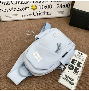 Detail of light blue nylon sling bag with CHUANGMI logo on brown textured fabric
