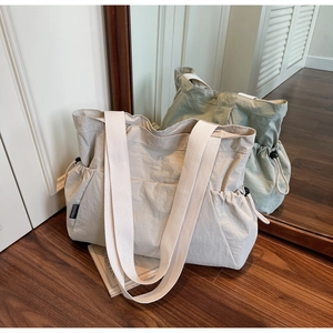 Detail view of large canvas tote bags in beige and green featuring side drawstring accents
