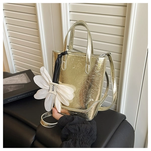Detailansicht goldene Handtasche mit weißem Blumenanhänger und verstellbarem Riemen