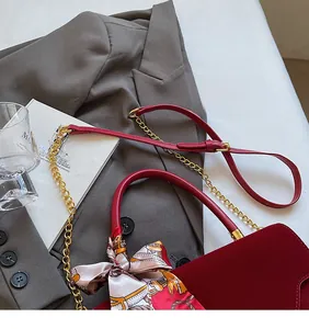Detail of burgundy bridal handbag with silk scarf handle and golden chain on a grey suit