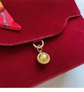 Detail of red velvet handbag with golden textured pendant and elegant printed silk scarf