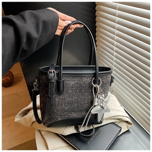 Détail du sac seau en tweed gris foncé avec poignées en cuir noir et breloque étoile