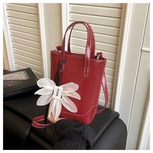 Detailansicht der roten Hochglanz-Handtasche mit Kontrastnähten und Blumenanhänger