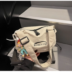 Detail of beige nylon crossbody bag with black BANATU logo and cute pendant on stairs