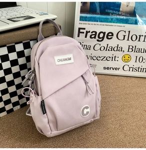 Detail of light purple nylon sling bag with knotted zippers and side pocket on a rug