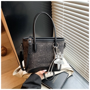 Détail du sac seau en tweed avec breloque étoile et bordures en cuir sur surface texturée