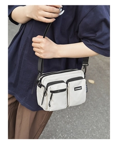 Detail of a beige nylon crossbody bag featuring double front zipper pockets and black strap