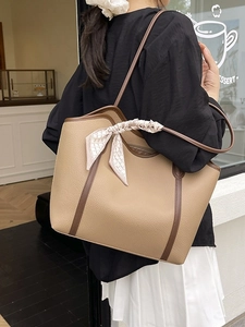 Large camel tote bag with silk scarf on handle worn by a model in a street style setting