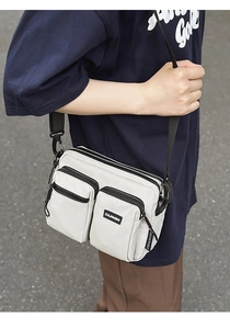 Outdoor view of a white waterproof crossbody bag with multiple pockets and a wide strap
