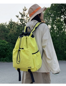 Macro detail of a bright yellow water-resistant drawstring backpack on a female model