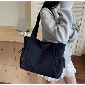 Detail of minimalist black nylon tote bag showing side drawstring pocket for daily commute