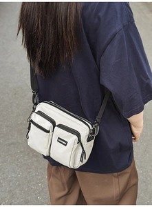 Outdoor shot of a beige nylon crossbody bag with multi-zipper pockets and black strap