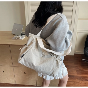 Detail of light beige large tote bag with adjustable drawstring side pocket and wide strap