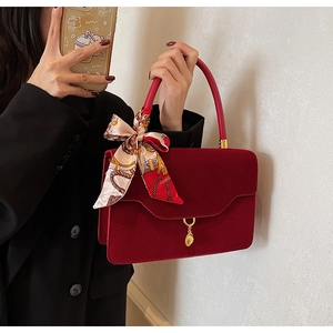 Detail of red bridal handbag with matte texture, gold charm and printed silk scarf handle