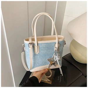 Détail du sac seau en denim bleu avec bordure en cuir beige et breloque étoile argent