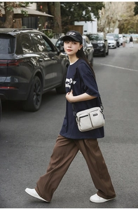 Outdoor street style view of casual beige multi-pocket nylon crossbody bag and blue t-shirt