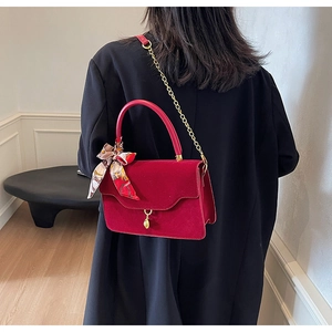 Detail of red velvet handbag with gold chain strap and decorative silk scarf detail