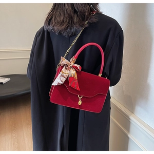 Detail of red bridal handbag with gold chain, silk scarf handle, and suede finish texture