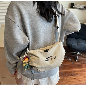 Detail of beige nylon crossbody bag featuring BANATU logo and cartoon doll charm