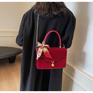 Detail of red velvet bridal bag with golden chain and silk scarf on a black coat