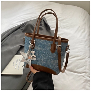 Détail du sac seau en denim avec bordures en cuir marron et breloques étoiles
