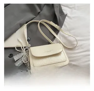 Détail du sac en cuir plissé blanc crème avec breloque perle et dentelle sur blazer