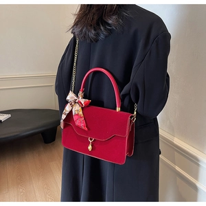 Detail of red velvet bridal handbag with golden chain strap and silk scarf accessory