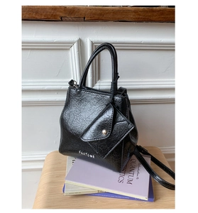 Detail of black patent leather handbag with detachable mini pouch and metal logo branding