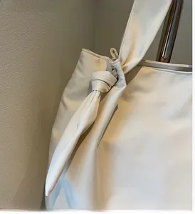 Detail of minimalist tote bag showing metal eyelet hardware and knotted shoulder strap