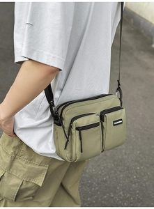 Detail of light green multi-pocket crossbody bag with adjustable black shoulder strap