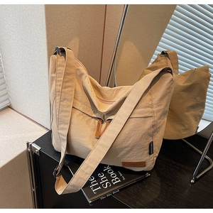 Grand sac hobo en toile avec large bandoulière et détail de marque devant un miroir