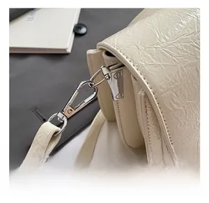 Gros plan des crochets en métal argenté et du cuir texturé de ce sac à bandoulière crème