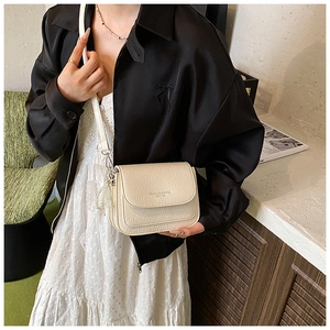Détail du sac bandoulière crème plissé avec breloque perle et lettrage mode