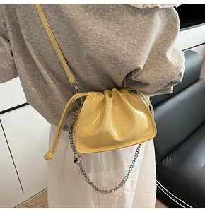 Detail of a bright yellow glossy drawstring bucket bag with silver chain and shoulder strap