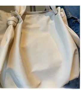 Detail of soft cream tote bag featuring stylish knotted handle and metal eyelet design