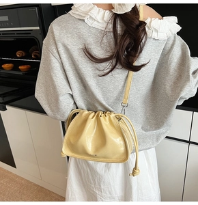 Detail view of yellow pleated cloud bucket bag with glossy finish and logo print