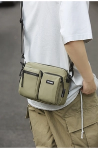 Detailed outdoor view of olive nylon crossbody bag featuring multiple zipper pockets and strap