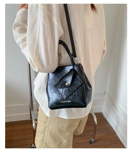 Detail of a black textured crossbody bag with a silver buckle and slender shoulder strap