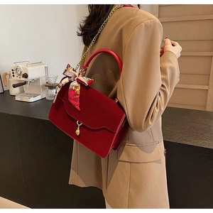 Detail of red velvet handbag with wave pattern flap, gold chain, and floral silk scarf