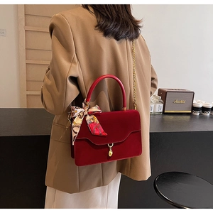 Detail of dark red suede handbag with elegant wave flap and decorative silk scarf