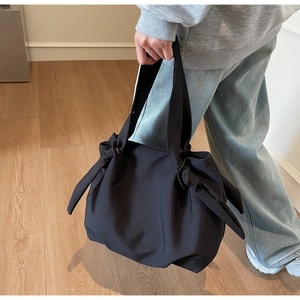 Detail of a large black tote bag featuring distinctive bow knot straps and durable matte fabric