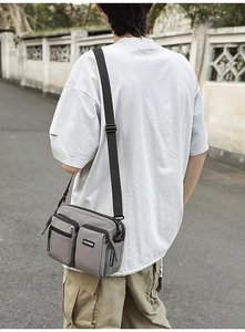 Detail of grey multi-pocket nylon crossbody bag worn by model in urban street setting