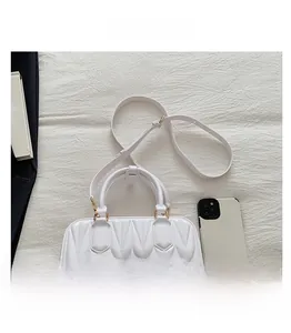 Detailed view of white quilted faux leather handbag with gold metal hardware and phone for size