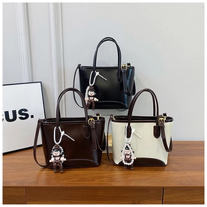 Détails de trois sacs cabas bicolores en noir, café et beige avec des pendentifs perle