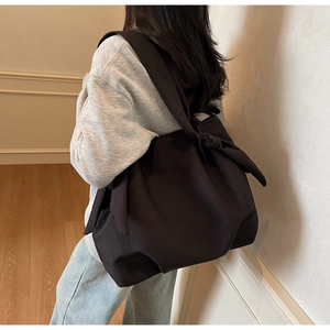 Detail of black tote bag with oversized decorative bow knot on wide shoulder strap