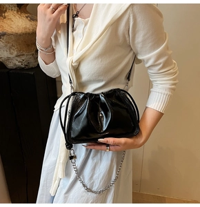 Detailed view of black patent leather drawstring bucket bag with silver chain and logo