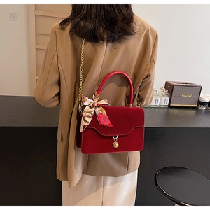 Detail of red velvet handbag with gold chain strap and decorative floral silk scarf handle