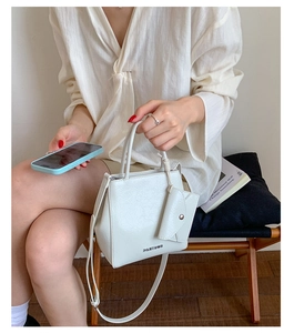 Close-up of white textured leather crossbody bag with silver logo and mini coin purse